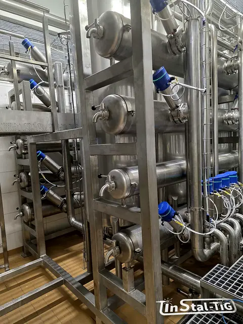 Zawory z niebieskimi napędami i rury poprowadzone wzdłuż stelaża przy filtrach